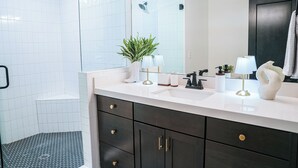 Un baño moderno con tocador blanco, armarios oscuros, un espejo grande y una zona de ducha con azulejos de diseño azul.