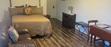 A bedroom with a bed, a desk, a chair, a leather sofa, a ceiling fan, and a TV mounted on the wall.