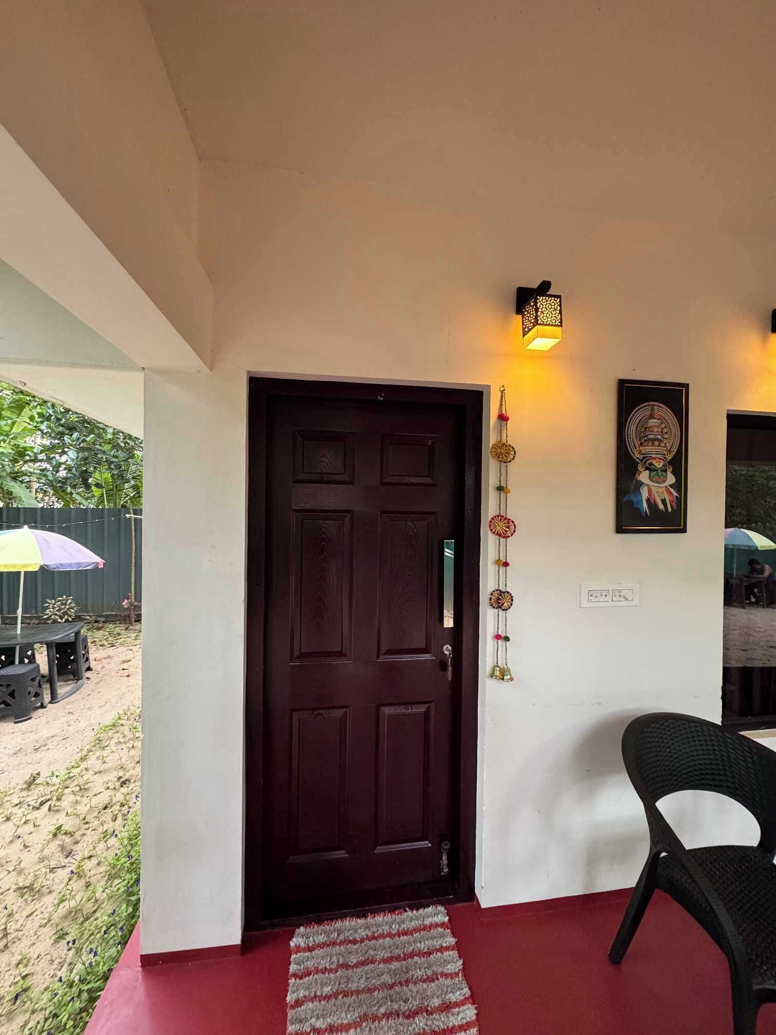 A dark wooden door with a textured surface, a small rug on the floor, a wall-mounted light fixture, and a framed picture.