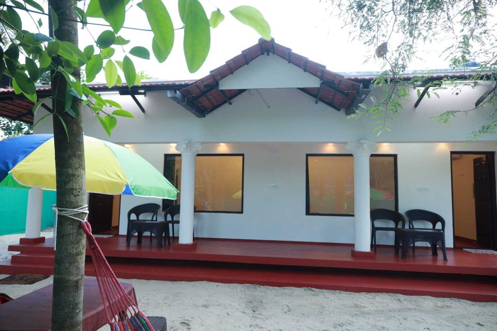 Um edifício com telhado vermelho, paredes brancas e varanda coberta com cadeiras de plástico.