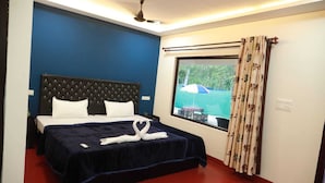 Hotellihuone, jossa on sänky, ikkuna verhoilla ja kattotuuletin.