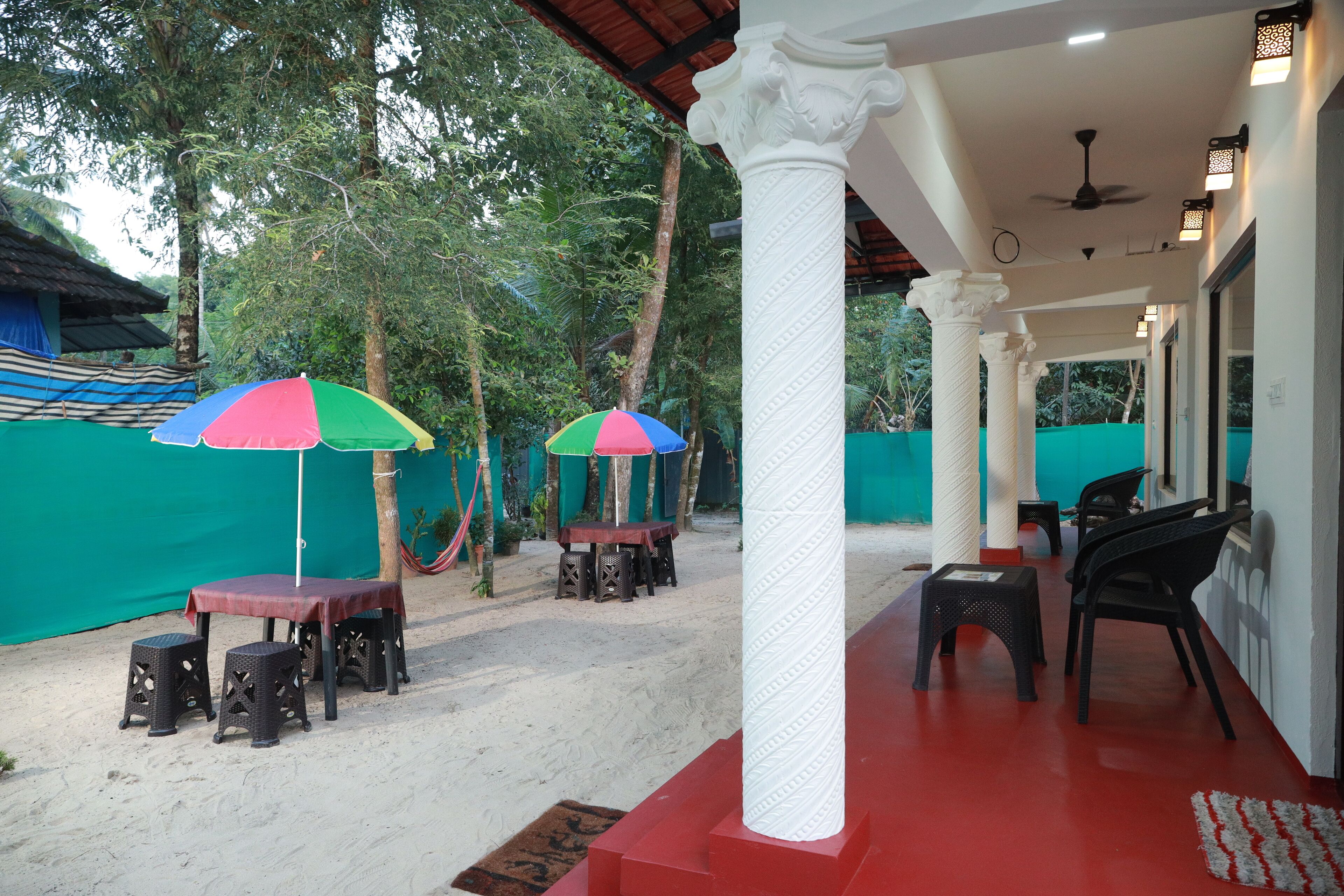 An outdoor seating area with tables and chairs, a covered section with a ceiling fan, and a green fence in the background.
