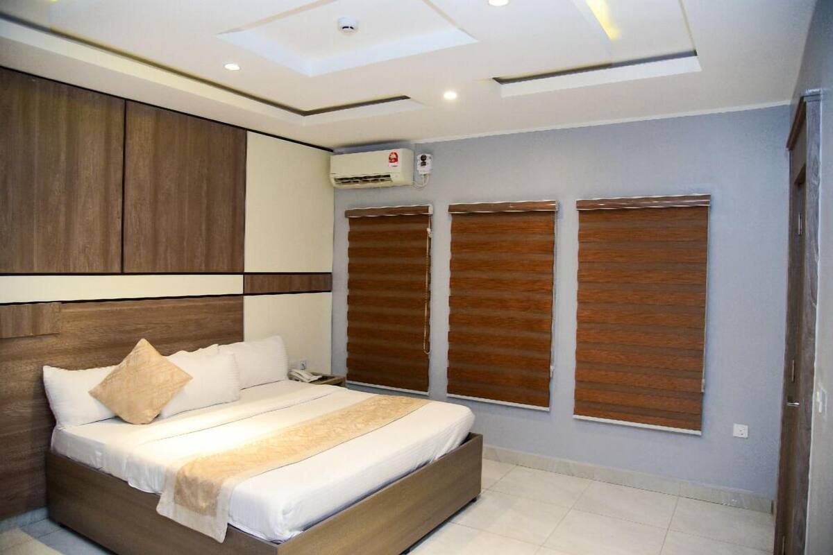 Une chambre à coucher moderne avec une tête de lit en bois, un lit recouvert de linge de maison blanc et un ventilateur de plafond.