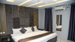 A modern hotel room with a large bed, a built-in headboard, a bedside table, and a large mirror. - Hotel De Alommah Kubwa Abuja Nigeria (Abuja)