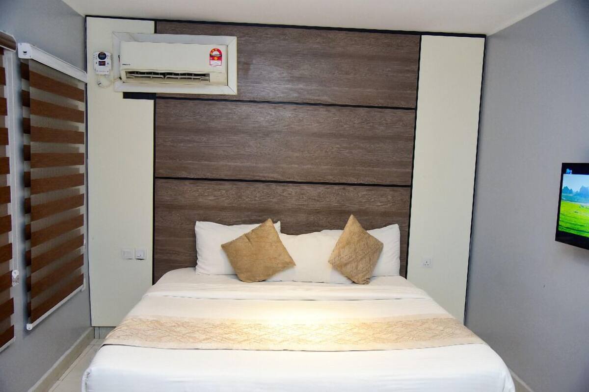 Une chambre d’hôtel avec un lit, un climatiseur fixé au mur et un téléviseur mural.