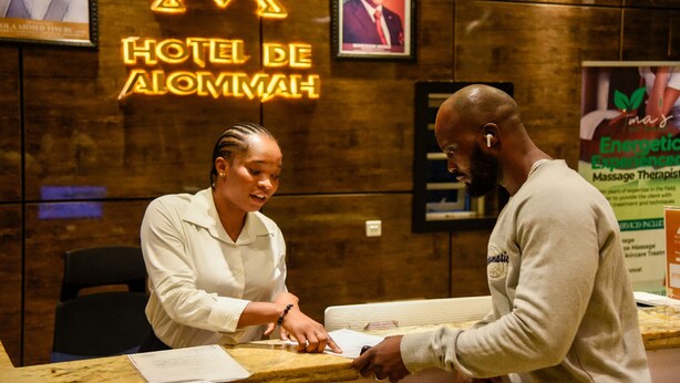 A hotel reception desk with a neon sign reading "HOTEL DE ALOMMAH". - Hotel De Alommah Kubwa Abuja Nigeria (Abuja)