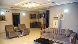 A modern living room with a sofa, two armchairs, a coffee table, and a kitchen area in the background. - Hotel De Alommah Kubwa Abuja Nigeria (Abuja)