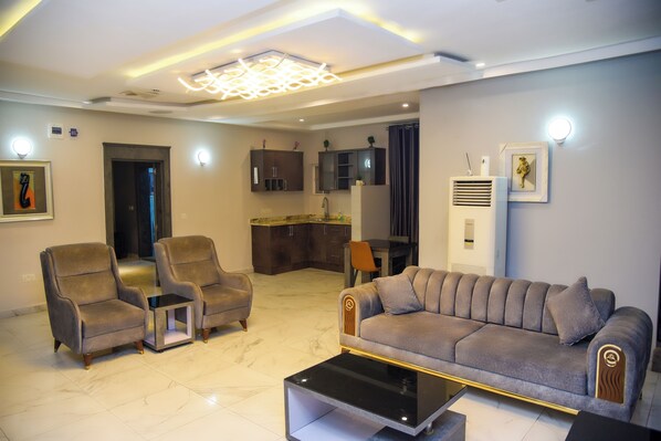 A modern living room with a sofa, two armchairs, a coffee table, and a kitchen area in the background. - Hotel De Alommah Kubwa Abuja Nigeria (Abuja)
