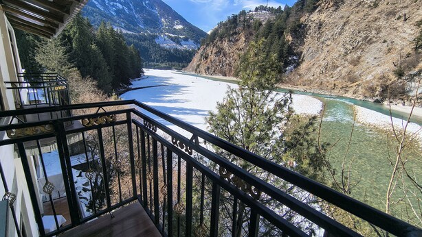 Un balcon avec vue sur une rivière, des montagnes et une zone boisée.