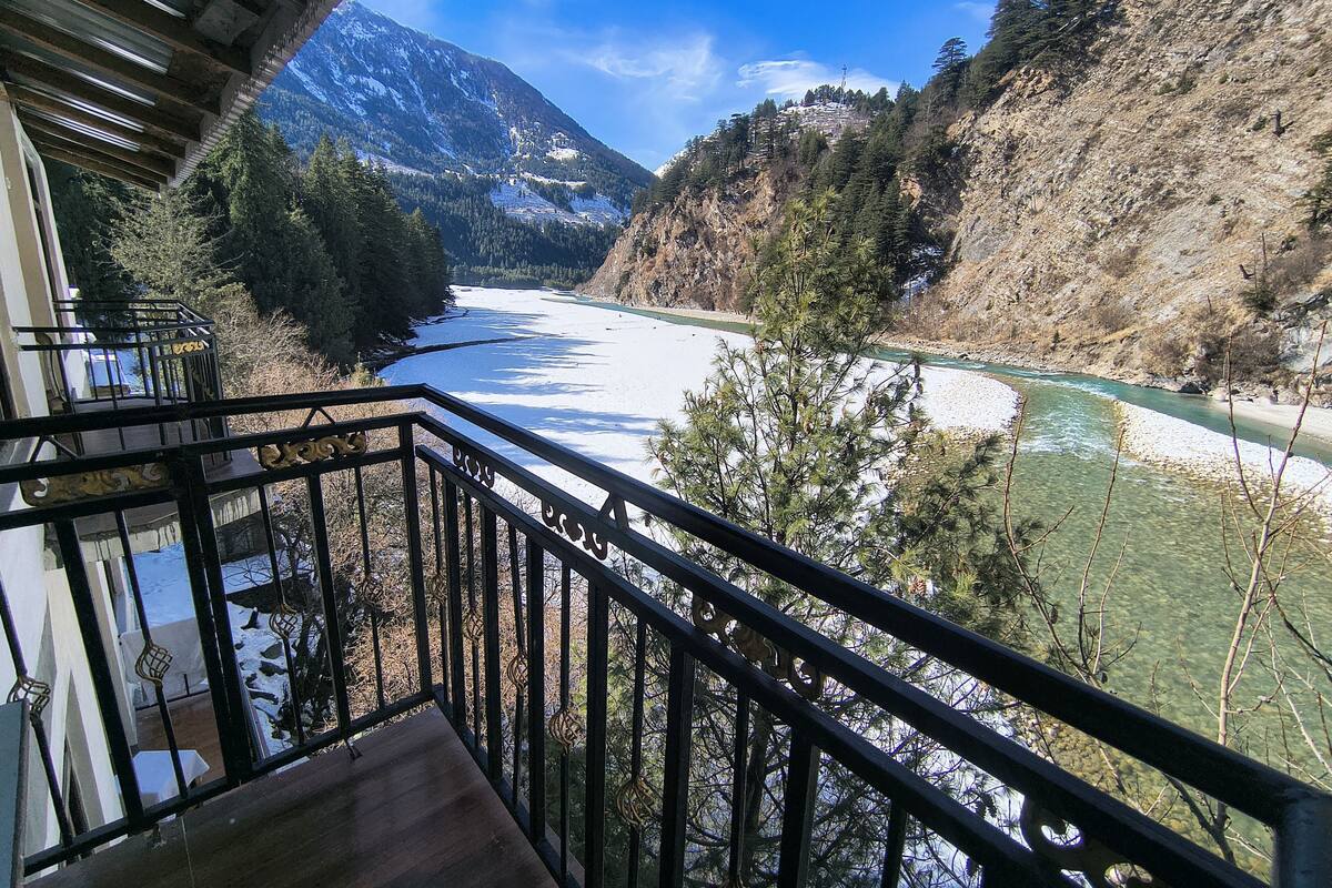 Un balcon avec vue sur une rivière, des montagnes et une zone boisée.