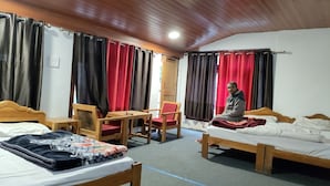 Une chambre d’hôtel avec deux lits, une table en bois, une chaise et une personne assise sur l’un des lits.