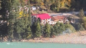 Un bâtiment avec un toit rouge, entouré d’une forêt dense et bordé par une rivière.
