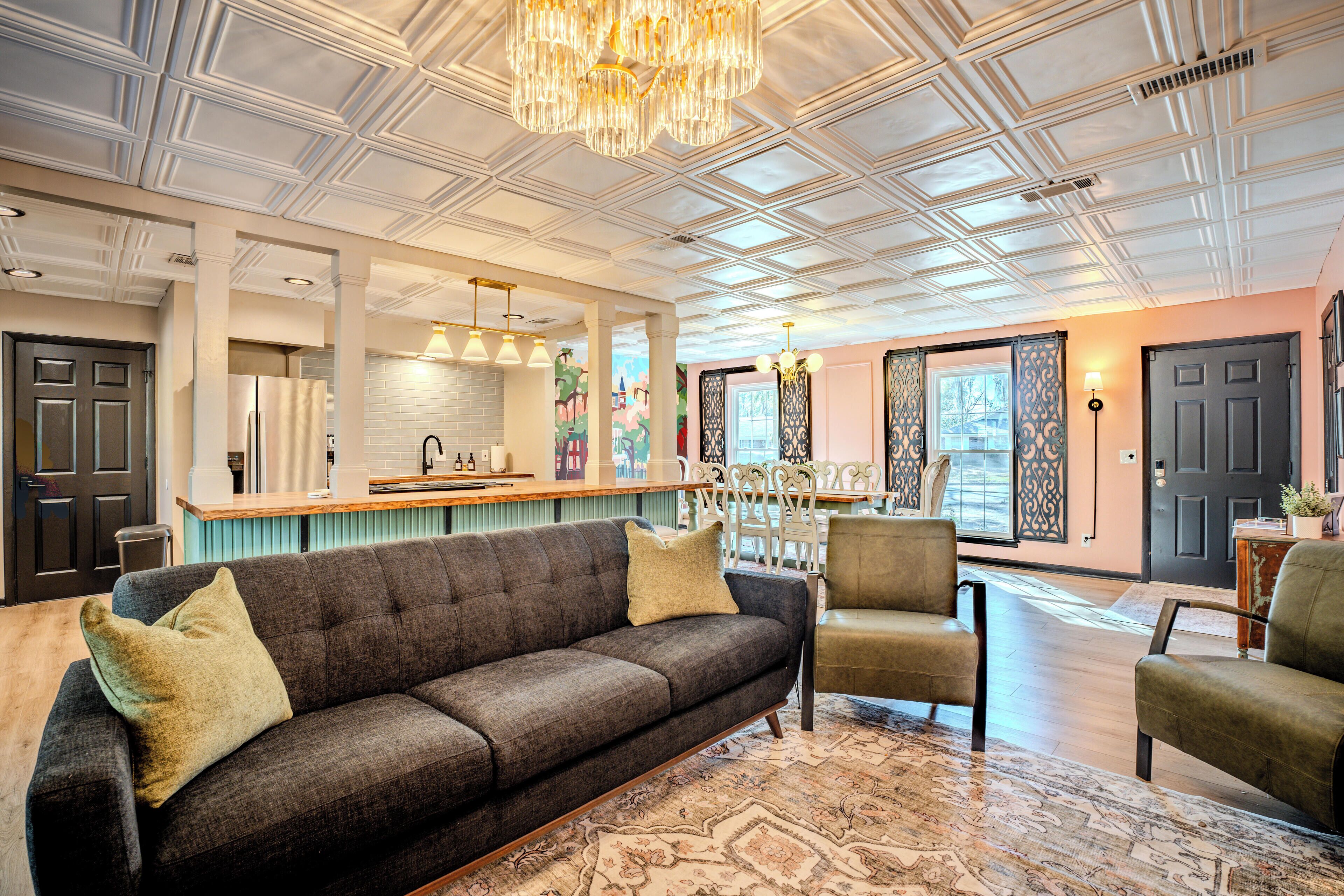 A spacious living area with a dark grey sofa, a patterned rug, and a chandelier.