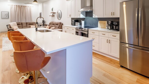 Une cuisine moderne dotée d’un îlot central, d’appareils électroménagers en acier inoxydable et d’un coin salon avec des chaises orange.