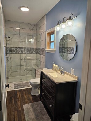 A bathroom with a glass shower enclosure, a toilet, a vanity with a sink, and a mirror. - 3-bedroom house in enjoyable Laurel with WiFi, AC (Laurel)