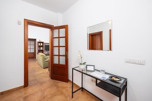 A hallway with a wooden door, a glass desk with a laptop, a potted plant, and a framed certificate.