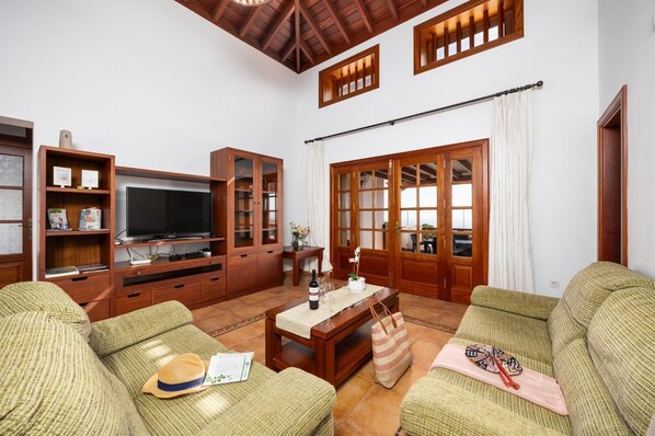 A living room with a TV, wooden cabinets, and two green sofas.