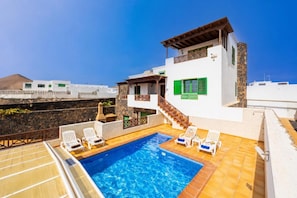 Un área de piscina en la azotea con una piscina azul cristalina, paredes blancas y contraventanas verdes.