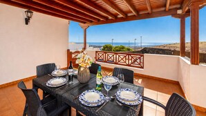 A covered outdoor dining area with a table set for four, a vase of flowers, and a view of the sea. - Casa Morro Blanco - Four Bedroom Villa, Sleeps 8 (Conil)
