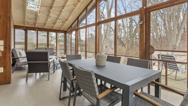 A spacious indoor area with a large table and chairs, large windows, and a wooden ceiling structure. - Stylish & Spacious Home | Hot Tub & 3-Season Deck (Douglas)