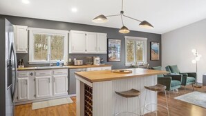 A modern kitchen with white cabinets, a wooden island with stools, and a pendant light fixture. - Stylish & Spacious Home | Hot Tub & 3-Season Deck (Douglas)