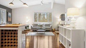 A modern living room with a sofa, coffee table, and a dining area with a wooden bar. - Stylish & Spacious Home | Hot Tub & 3-Season Deck (Douglas)