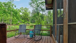 A wooden deck with two rocking chairs and a blue planter, overlooking a forested area. - Stylish & Spacious Home | Hot Tub & 3-Season Deck (Douglas)