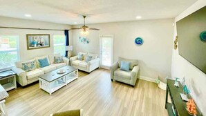 A spacious living room with a ceiling fan, a large window, and a flat-screen TV mounted on the wall. - Winter monthly rates 3000 fully furnished  (Panama City Beach)