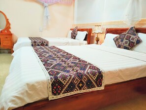 A hotel room with two beds, each with a white bedspread and a colorful, patterned throw blanket. There is a wooden nightstand with a mirror and a lamp between the beds. - Nguyen Dang Guesthouse  (Sa Pa)