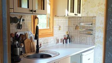 A compact kitchen with wooden beams, white cabinets, and a small trash bin.