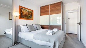 Una habitación de hotel moderna con una cama grande, un cuadro en la pared y una puerta a la derecha.