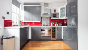 Una cocina moderna con armarios grises, un salpicadero rojo, electrodomésticos de acero inoxidable y suelo de madera.