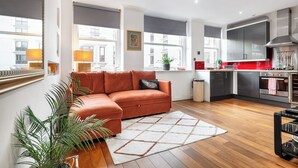 Una sala de estar moderna con un sofá seccional, una cocina con electrodomésticos de acero inoxidable y ventanas amplias que ofrecen vistas de la ciudad.