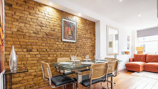 Un comedor con pared de ladrillo, mesa de vidrio y sillas modernas.