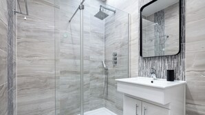 Un baño moderno con ducha envuelta en vidrio, un lavabo blanco y una pared con diseño de mármol.