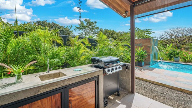 Ein Außenbereich mit Küche, Grill, Spüle und Blick auf einen Swimmingpool.