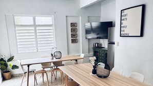 Ein Essbereich mit Holztisch, weißen Stühlen und einem an der Wand befestigten Fernseher.
