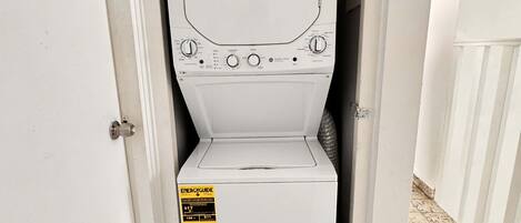 A compact, white washing machine in a narrow hallway with a door on one side.