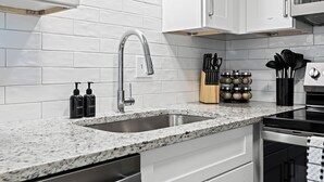 A modern kitchen with white cabinetry, a granite countertop, a stainless steel sink, and a built-in oven. - New! Modern 2BR by Downtown Royal Oak | King Beds (Royal Oak)
