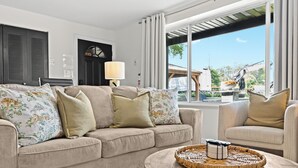A living room with a beige sofa, a round coffee table, and a view of the outside through a large window. - New! Modern 2BR by Downtown Royal Oak | King Beds (Royal Oak)