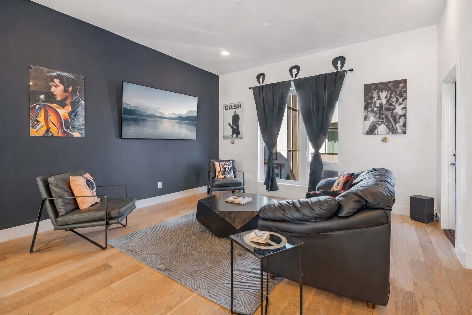 A modern living room with a black leather sofa, a coffee table, a black armchair, and a large TV.