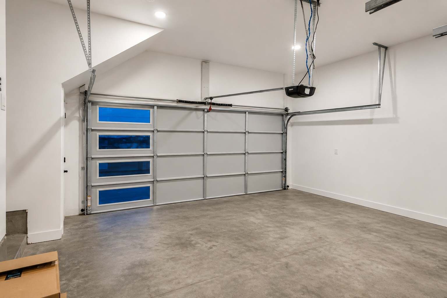 A garage with a metal door, a ceiling-mounted projector, and a concrete floor.