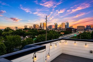 Terraza en la azotea con luces colgantes, con vistas a un horizonte urbano al atardecer.