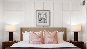 Une chambre d’hôtel avec un grand lit, deux lampes de chevet, un tableau encadré au mur et un plaid à motifs.