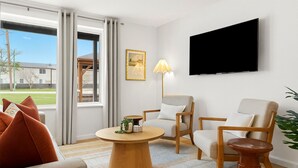 Un salon moderne avec un téléviseur à écran plat, deux fauteuils, une table basse ronde et un canapé.