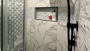 A bathroom with a glass shower enclosure, a black showerhead, and a marble backsplash.