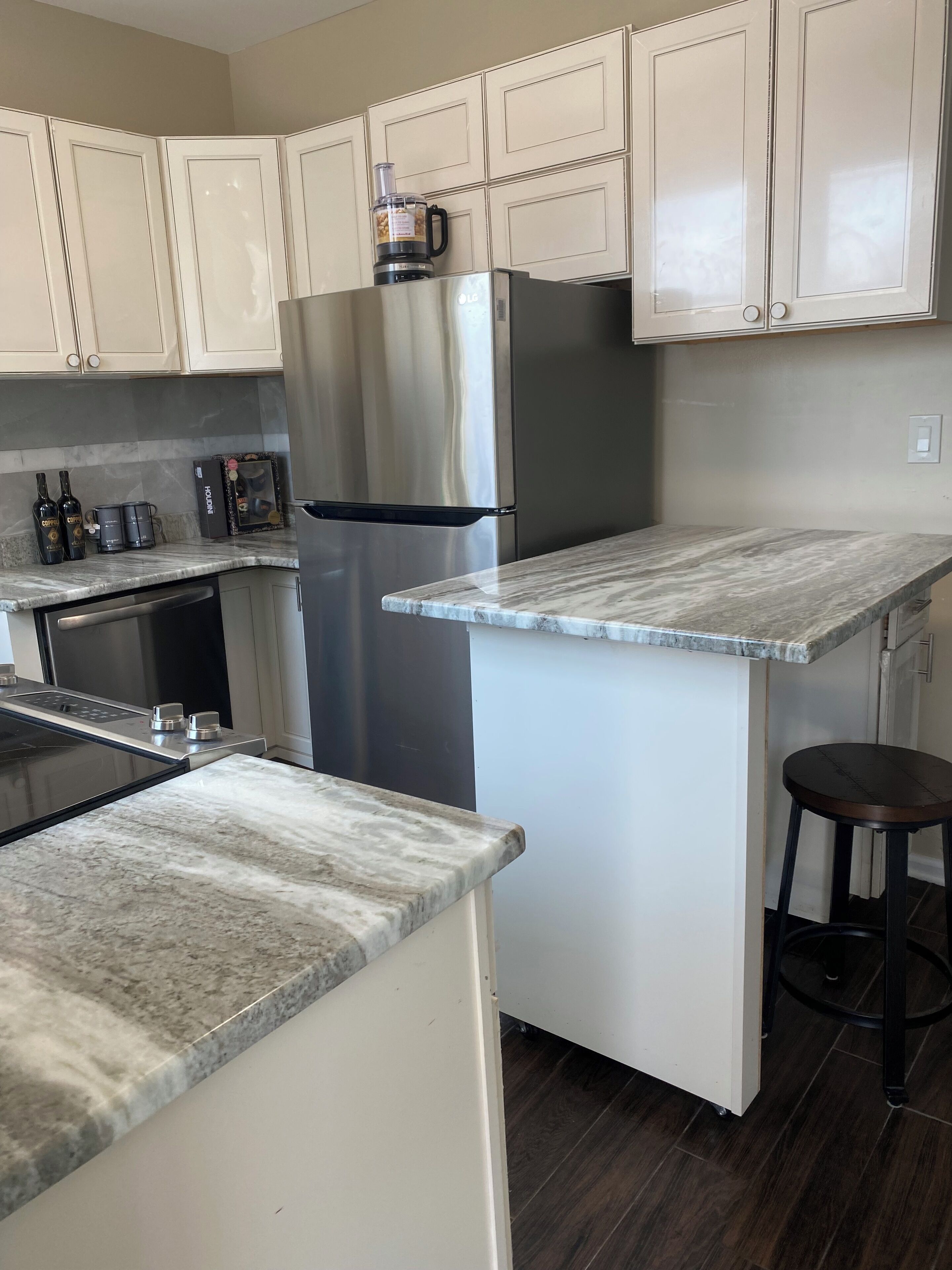 A modern kitchen with white cabinets, a stainless steel refrigerator, a built-in oven, and a marble countertop.