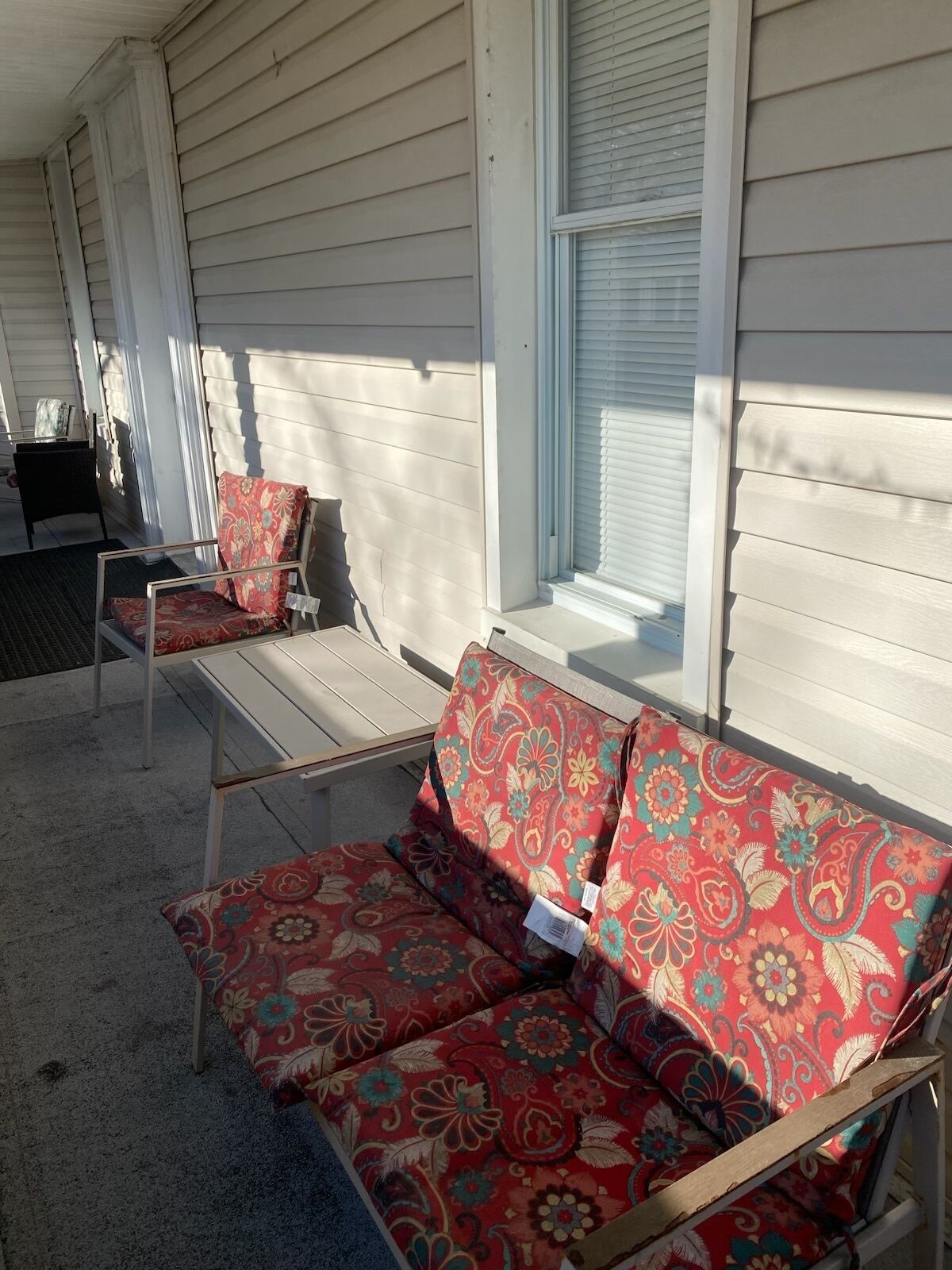 A covered porch with a white exterior, a bench, and a cushioned seating area.