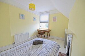 Une chambre à coucher comprenant un lit, un bureau, une chaise, un radiateur, une fenêtre avec des stores et un luminaire suspendu.