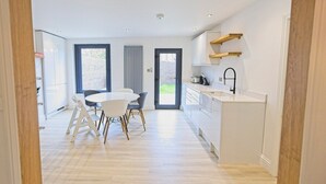 A modern kitchen with white cabinets, a dining area with a round table and chairs, and a view through a doorway to a living space.